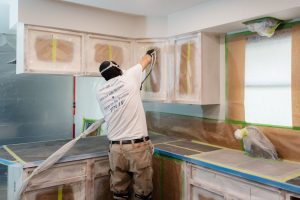 Professional Painter spraying kitchen cabinet bases.