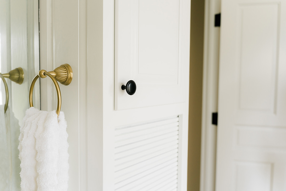 PMV - Blogs - Yes You Always Need Two Coats of Paint 1 White bathroom cabinet with a black cabinet pull and a gold hand towel holder with a white towel.