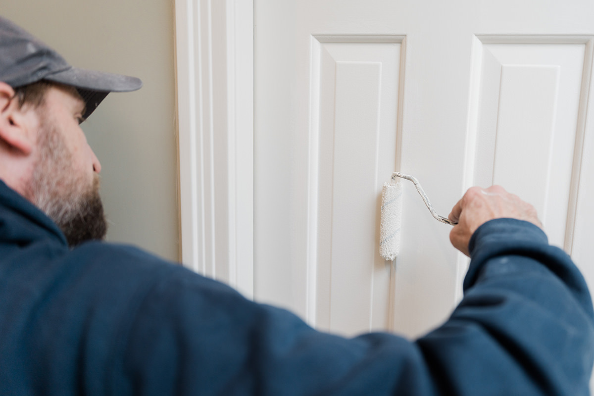 PMV - Blogs - Yes You Always Need Two Coats of Paint 2 Painter using a roller to put white paint on a door.