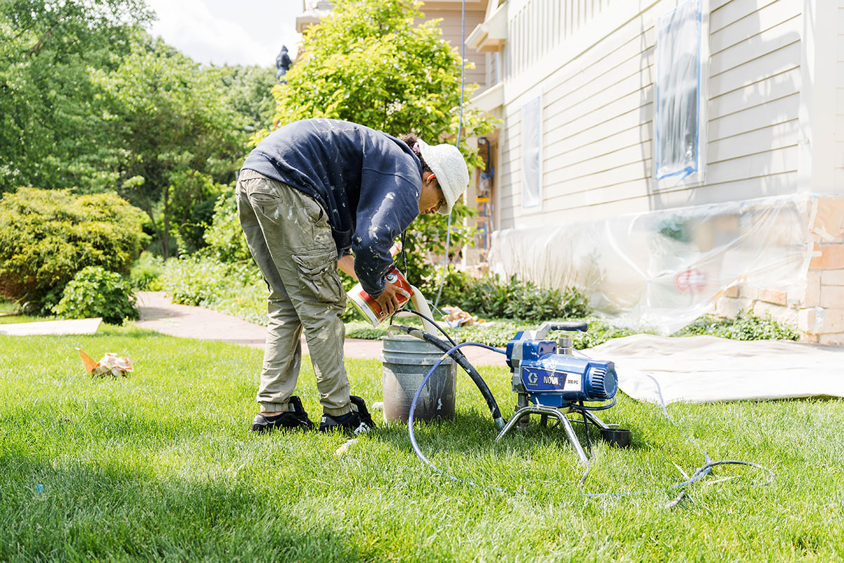House painter from PMV Painting refilling paint to paint the exterior of a house for a repaint project in Portage Michigan