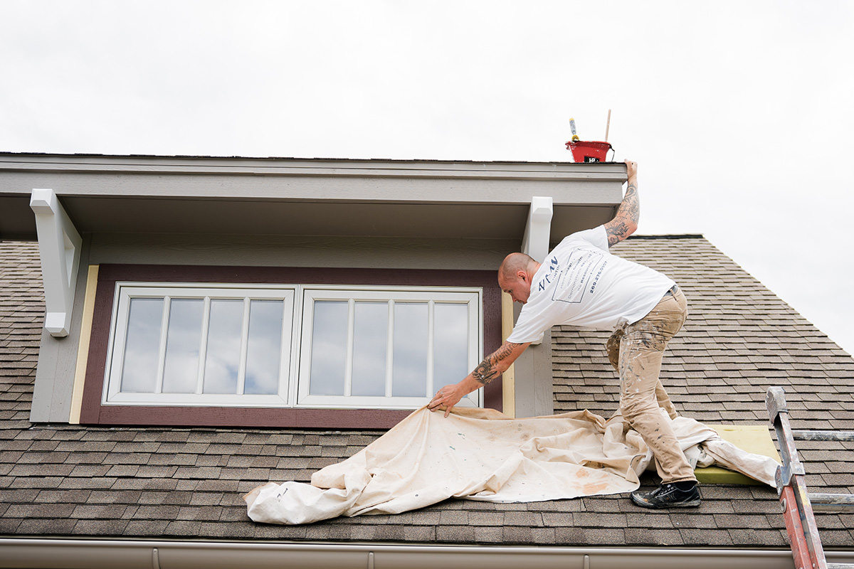 House painter from PMV Painting putting down a drop cloth before painting trim during an exterior house repaint project in Kalamazoo Michigan